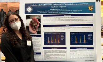 A Hispanic STEM grant recipient stands next to a research poster.