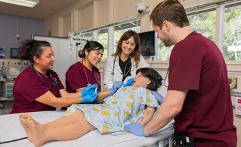 Nursing student and teacher around a hospital bed with mannequin