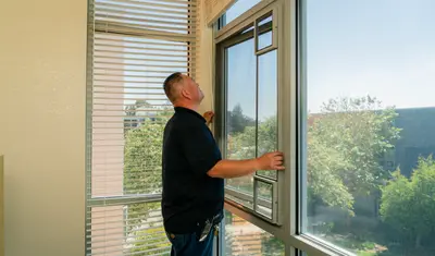A facilities management worker repairs a window in a student dorm
