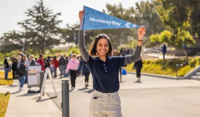 Student holding small Cal State Monterey Bay banner/flag