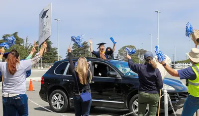 Excited graduate cheering from car while faculty and staff cheer her on